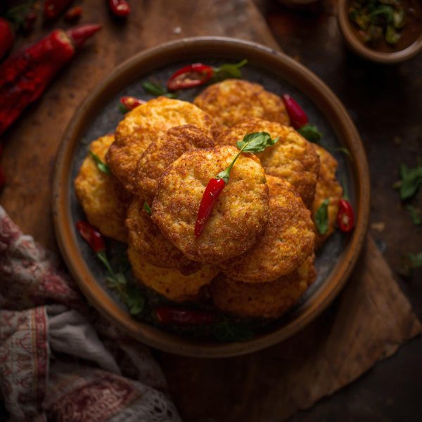 _Crispy golden karapoosa piled on a plate with red chili and curry leaves around, warm lighting, homely background_